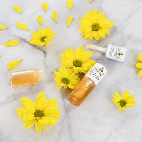 A'pieu Honey & Milk Lip Oil on marble with yellow flowers, Korean skincare Nederland, Me Time Groningen.