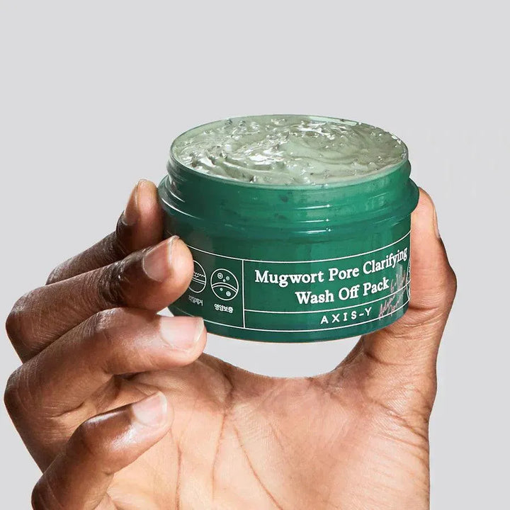 Hand holding AXIS-Y Mugwort Pore Clarifying Wash Off Pack, Korean skincare product in green jar.