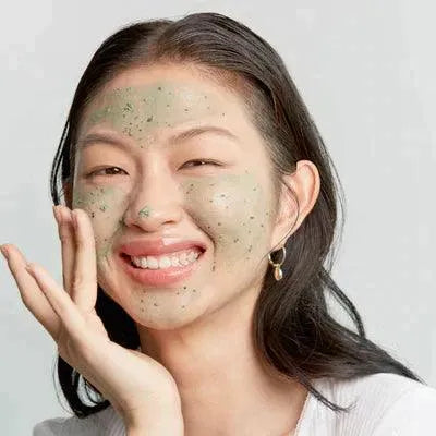 Smiling woman applying Axis-Y Mugwort Pore Clarifying Wash Off Pack, Korean skincare