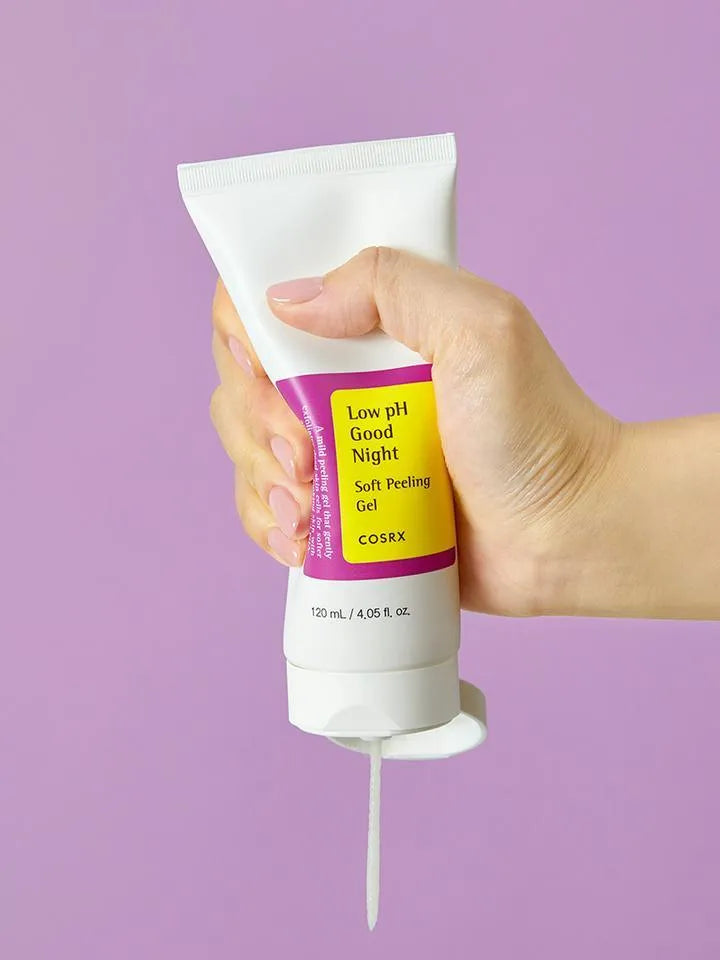 Hand holding COSRX Low pH Good Night Soft Peeling Gel tube against purple background