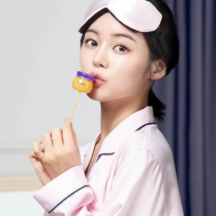 Woman in pink pajamas applying Frudia blueberry lip balm, Korean skincare product, Me Time Groningen