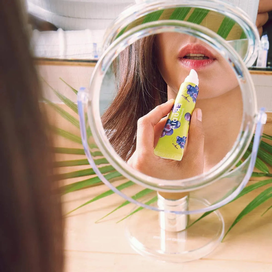 Woman applying Frudia Grape Honey Chu Lip Essence in front of a mirror, Korean skincare product at Me Time Groningen