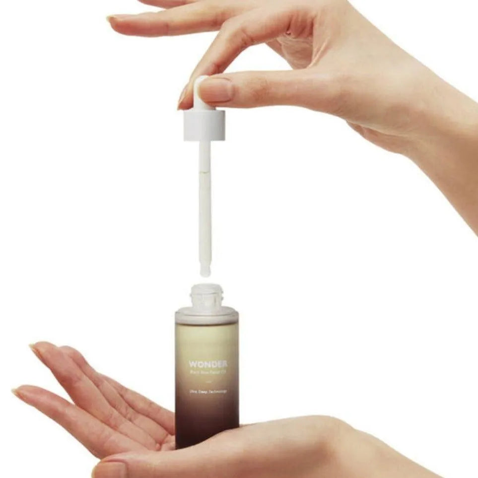 Hand holding Haruharu Wonder Black Rice Facial Oil bottle with dropper, Korean skincare