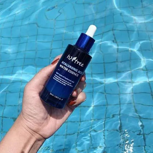 Hand holding Isntree Hyaluronic Acid Water Essence bottle over pool, Korean skincare Nederland