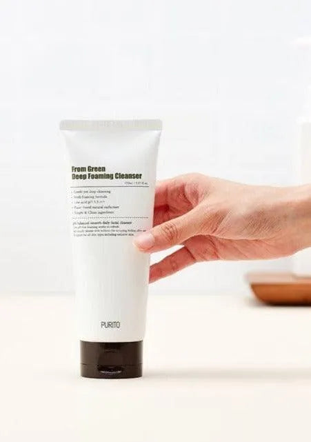 Hand holding Purito From Green Deep Foaming Cleanser on bathroom counter, Korean skincare product